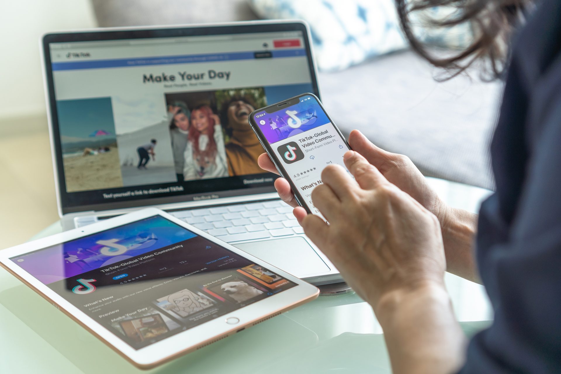 A woman holding a phone with TikTok open, surrounded by an iPad and laptop displaying TikTok.
