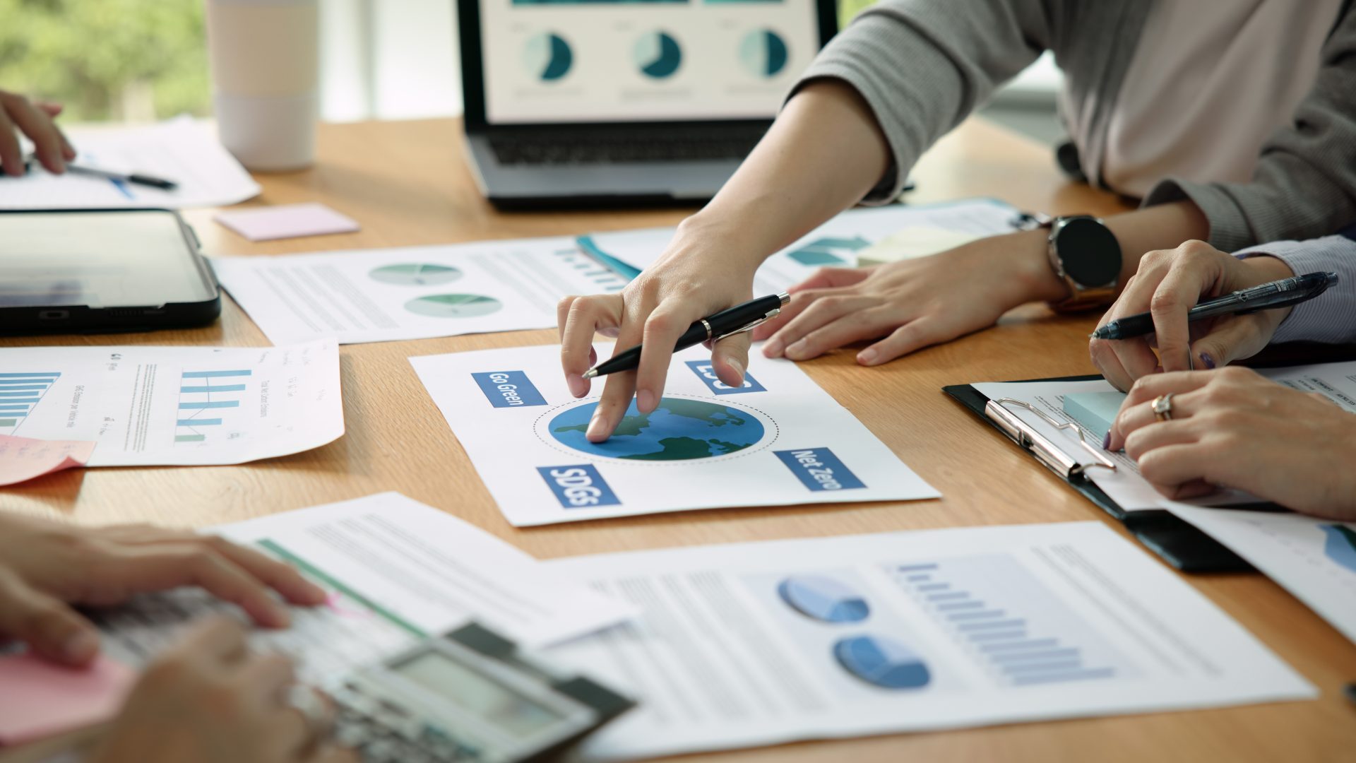 Person (ESG) pointing at documents arranged on a table during a collaborative planning session.