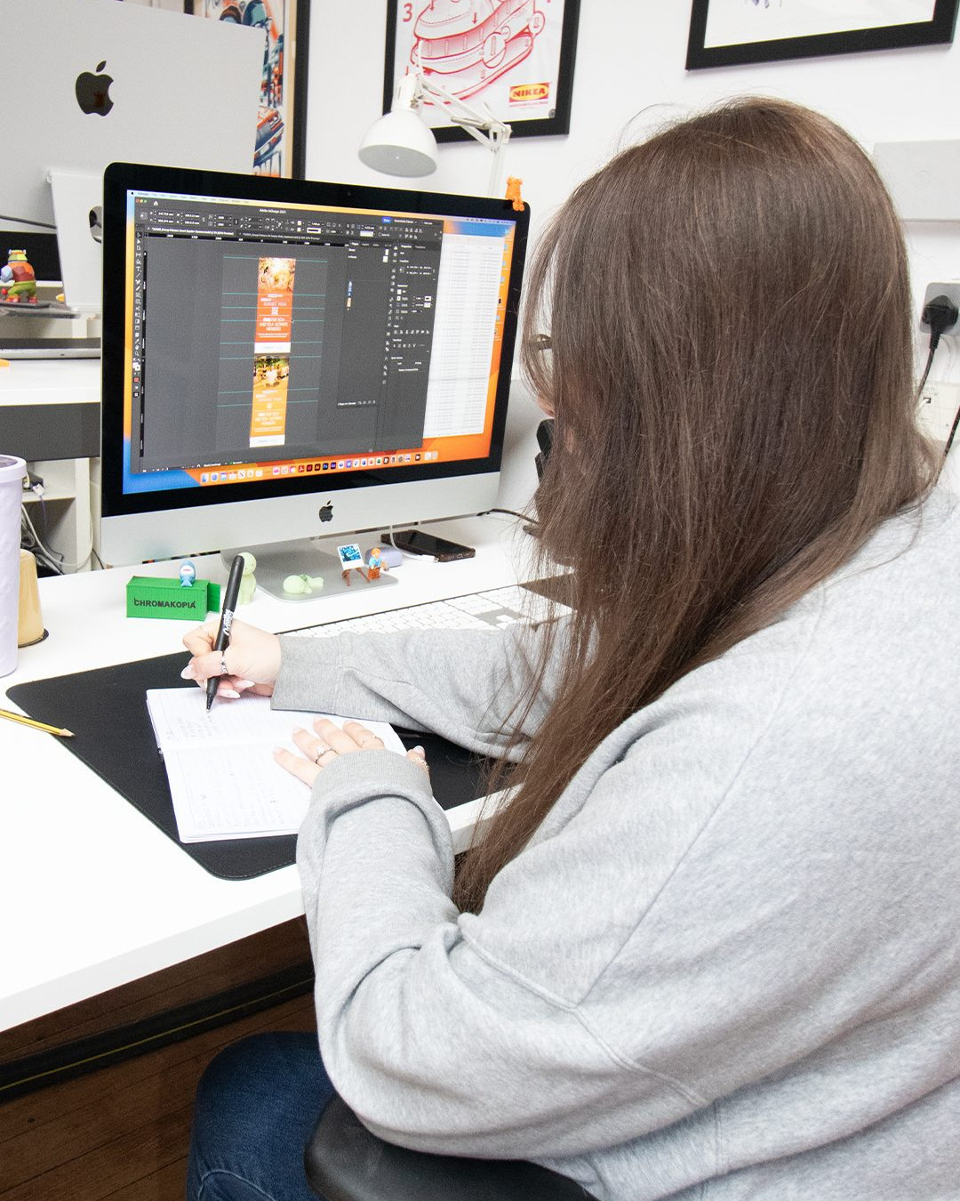 Gemma from Creative62 working at her MacBook while taking notes in a notebook.