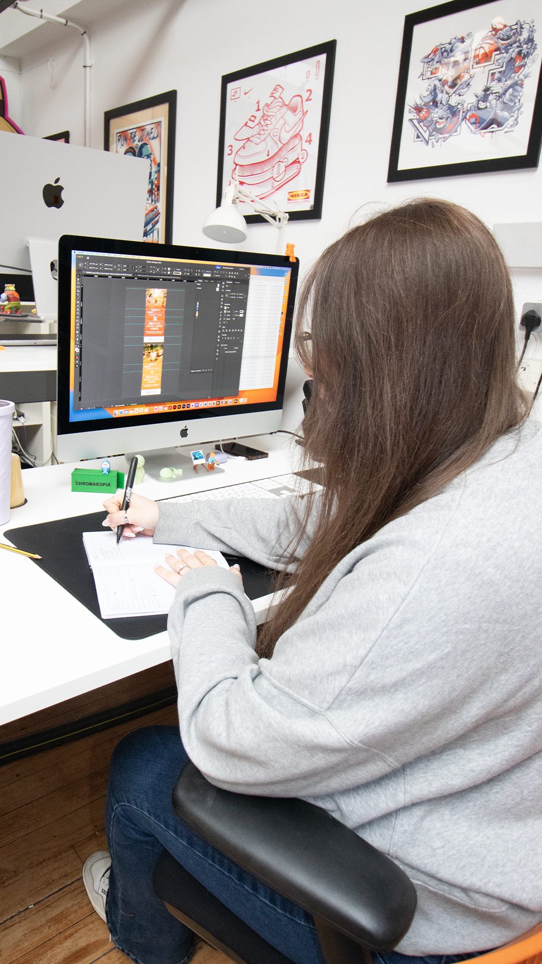 Gemma from Creative62 working at her MacBook while taking notes in a notebook.