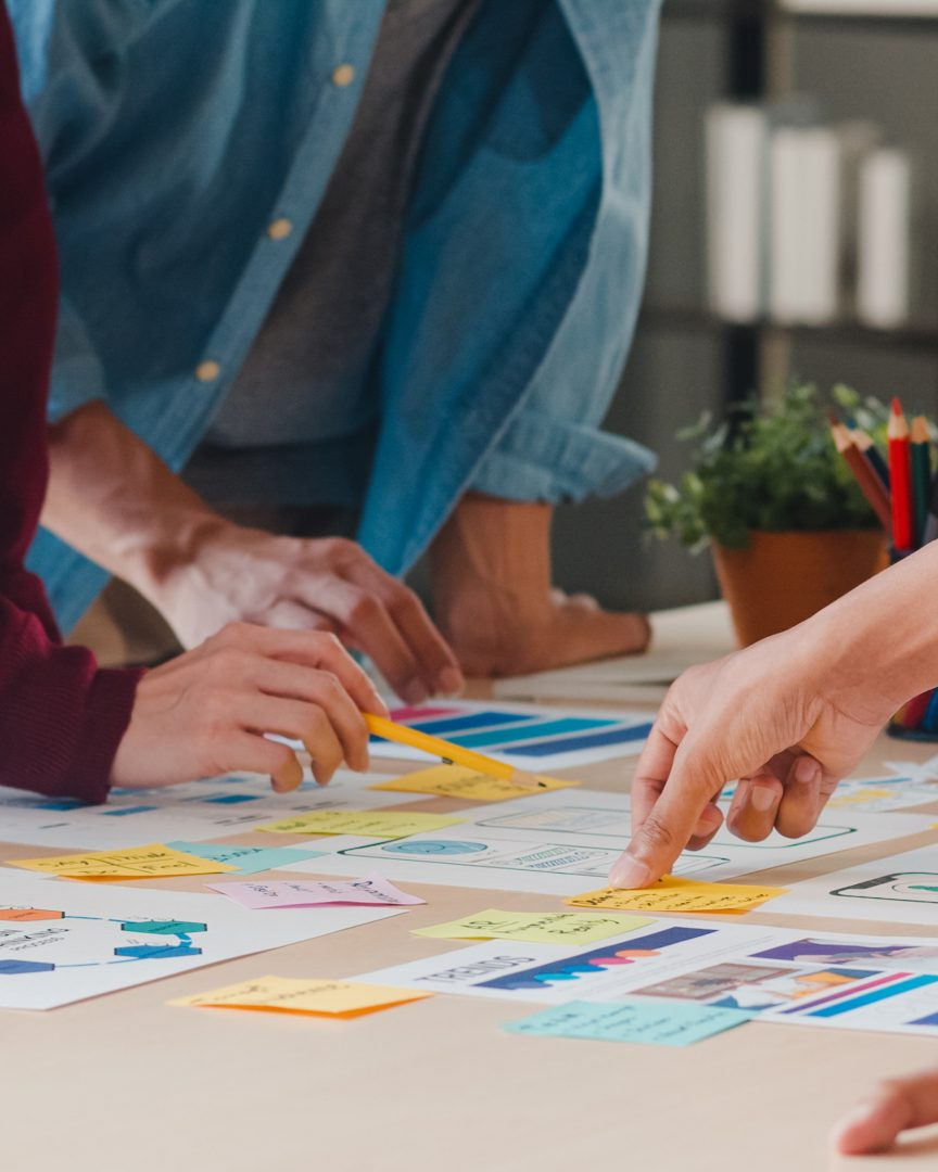People gathered around a table reviewing post-it notes and printed materials.