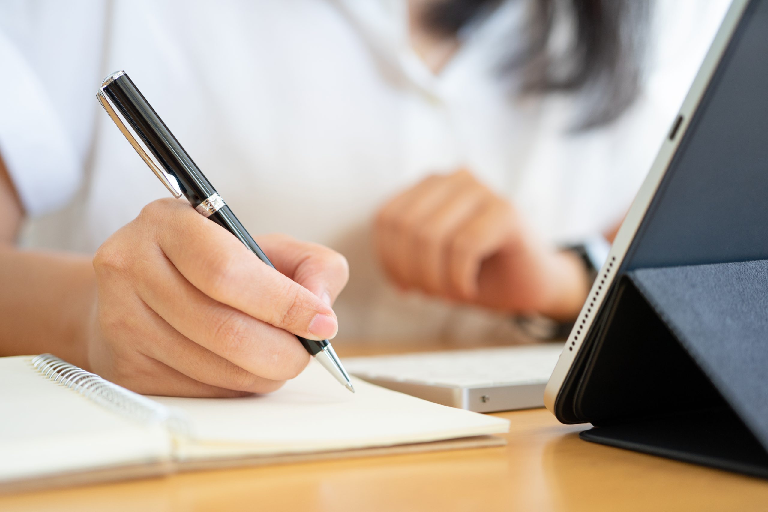 Professional taking notes during a marketing strategy and business planning session using a tablet and notebook.